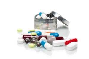 Tabletten ligen auf einem weissen Untergrund und in einer geöffneten Pillen-Dose, isoliert