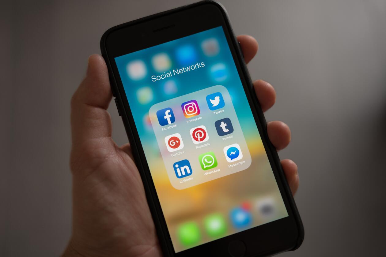 Hånd som holder smarttelefon med ikoner som representer apper for sosiale media.