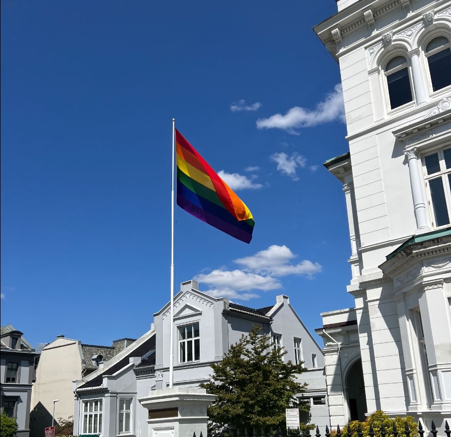 Bilde av rektoratbygningen på en finværs med prideflagget vaiende i vinden. 