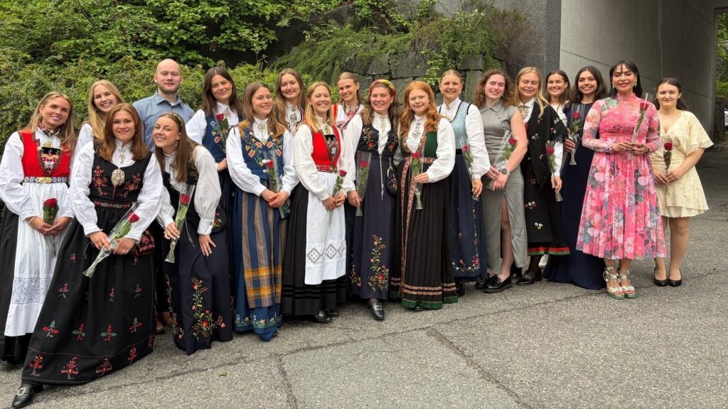 Gruppe bachelorstudenter i ernæring står samlet utendørs foran en bygning, flere iført bunad og holder roser under bachelorseremonien.